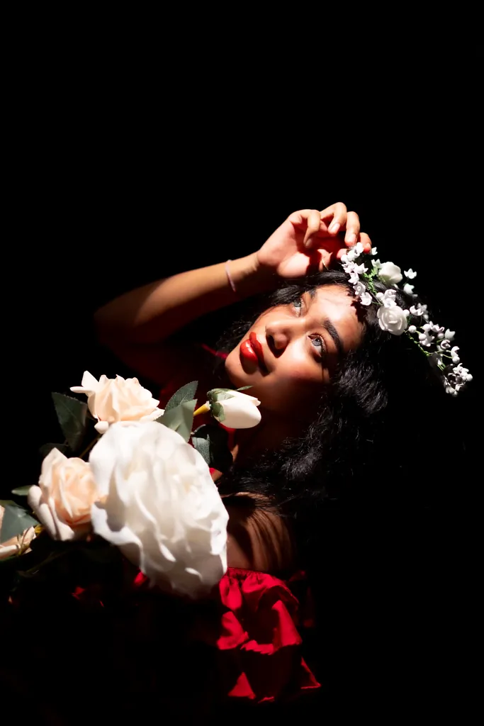 Model wearing a white flower crown, holding white roses against a black backdrop