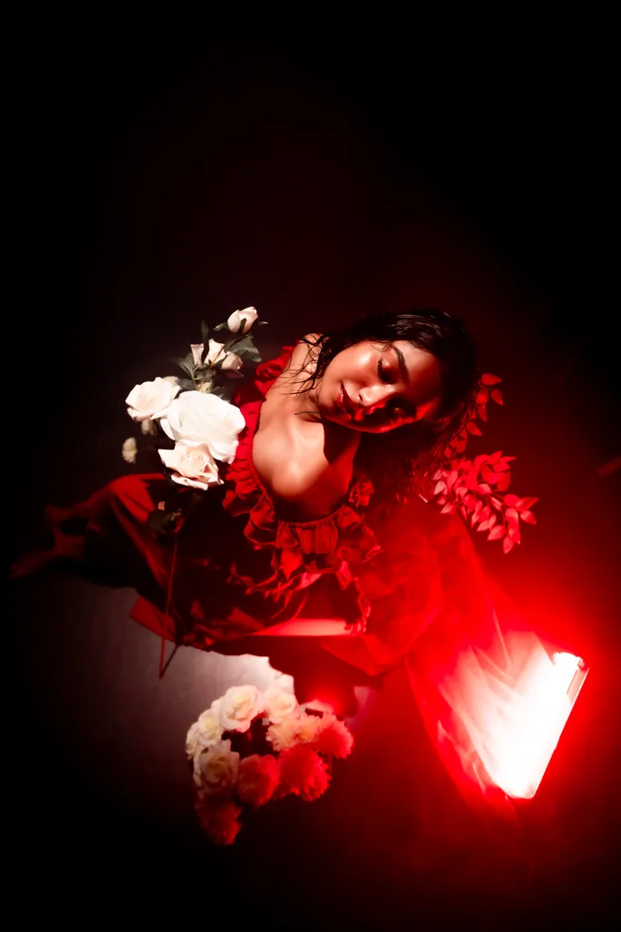 Model in red reclining among white roses under red light, shot from above