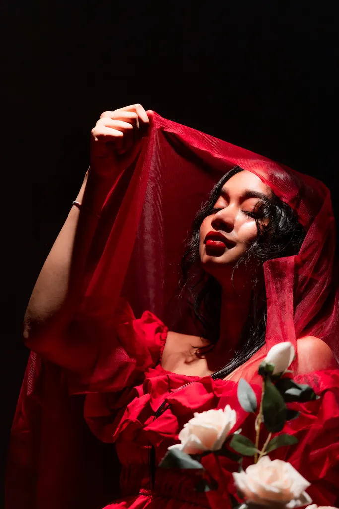 Model lifting a sheer red veil, surrounded by red and white roses