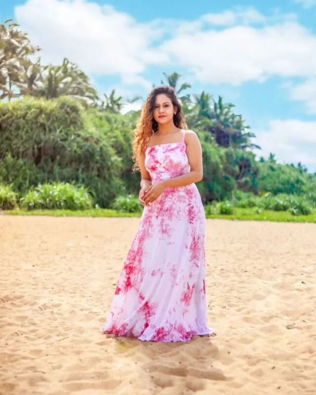 Model in a pink floral dress on a beach under a blue sky, photographed for Adare
