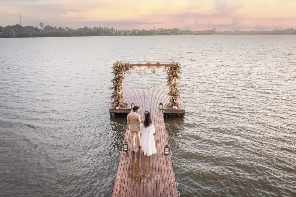 Aerial view of a couple at a floral arch at the end of a lakeside jetty at dusk