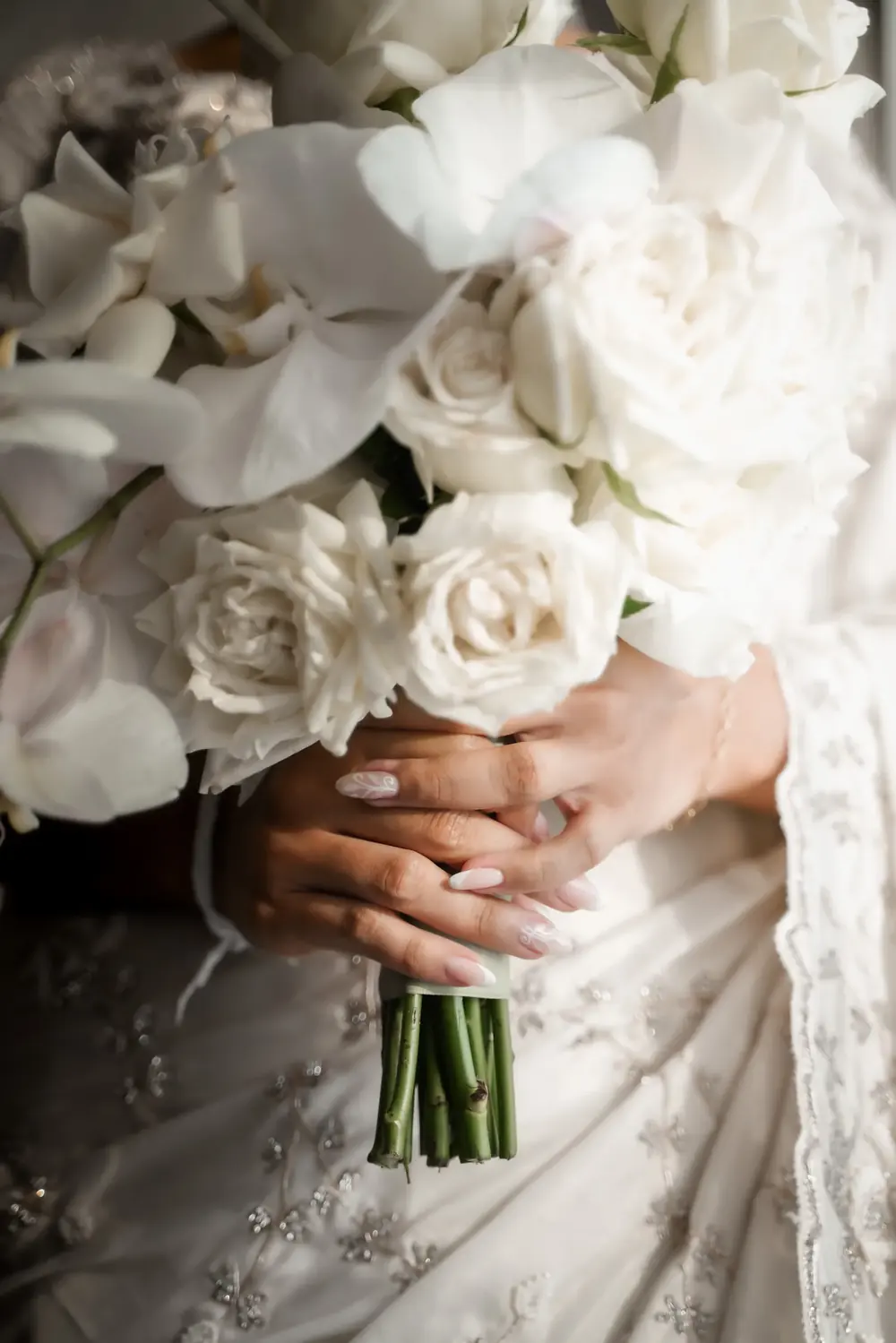 Close-up of a bride’s hands holding a white rose and orchid bouquet