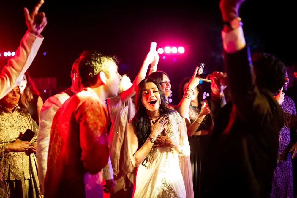 Guests laughing and dancing under pink stage lights at the sangeet