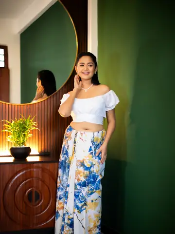 Model in a white top and blue floral maxi skirt beside a round mirror