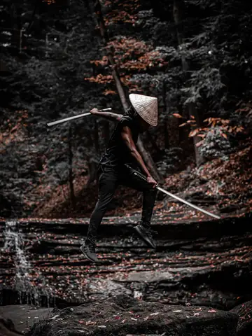 Person in a conical hat jumping with a sword in a forest