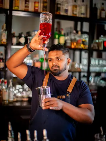 Bartender pouring a drink from height at a backlit bar