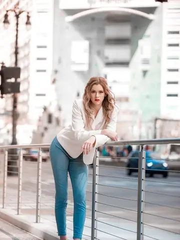 Woman in a white blazer posing beside a city railing