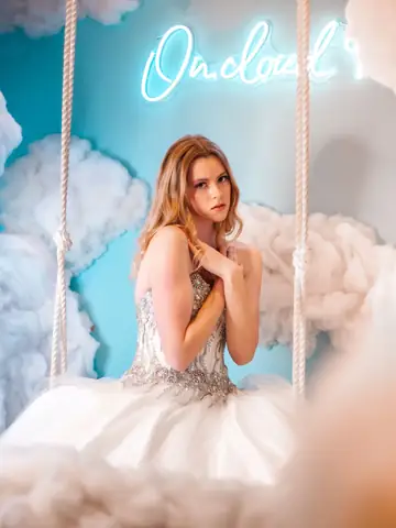 Woman in an elegant gown on a swing among cloud-like decor