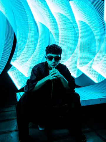 Stylish man in sunglasses beneath vibrant blue lights