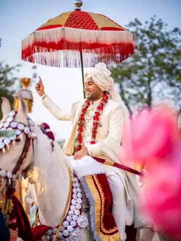 Groom in white and red riding a decorated white horse beneath a red ceremonial umbrella