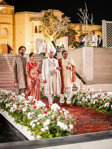 Couple and family at the top of a white-flower-lined aisle at night