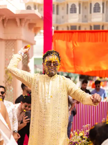 Groom in a gold kurta and sunglasses dancing at the haldi, face covered in turmeric