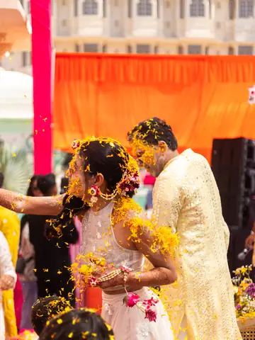 Bride and groom showered with marigold petals at their haldi, faces dusted with turmeric