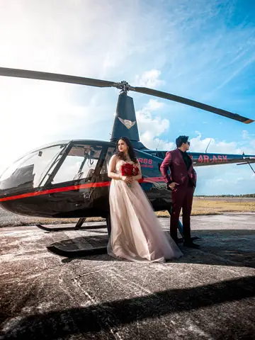 Couple in formal wear posing beside a helicopter on a helipad