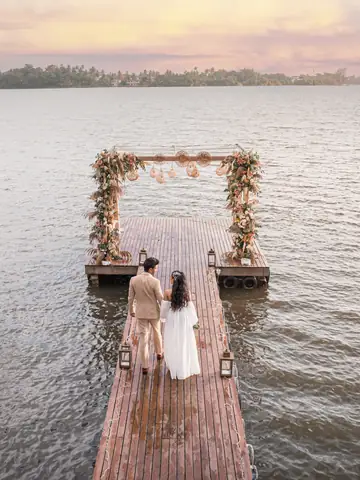Aerial view of a couple at a floral arch at the end of a lakeside jetty