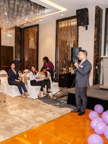 Speaker addressing guests at a ballroom event with pink balloons