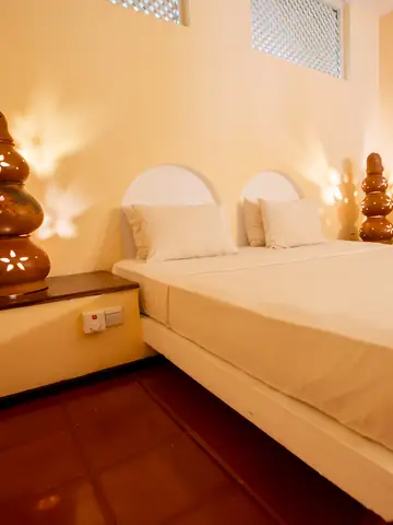 Hotel bedroom with a white double bed between two glowing clay lamps and terracotta floors