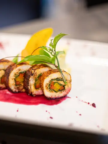 Plated dessert roll with fruit and sauce on a white plate