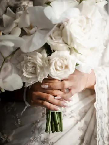 Close-up of a bride's hands holding a white rose and orchid bouquet