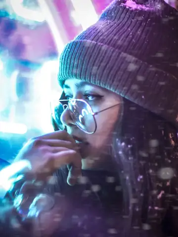 Woman wearing a beanie and glasses near neon lights in snow