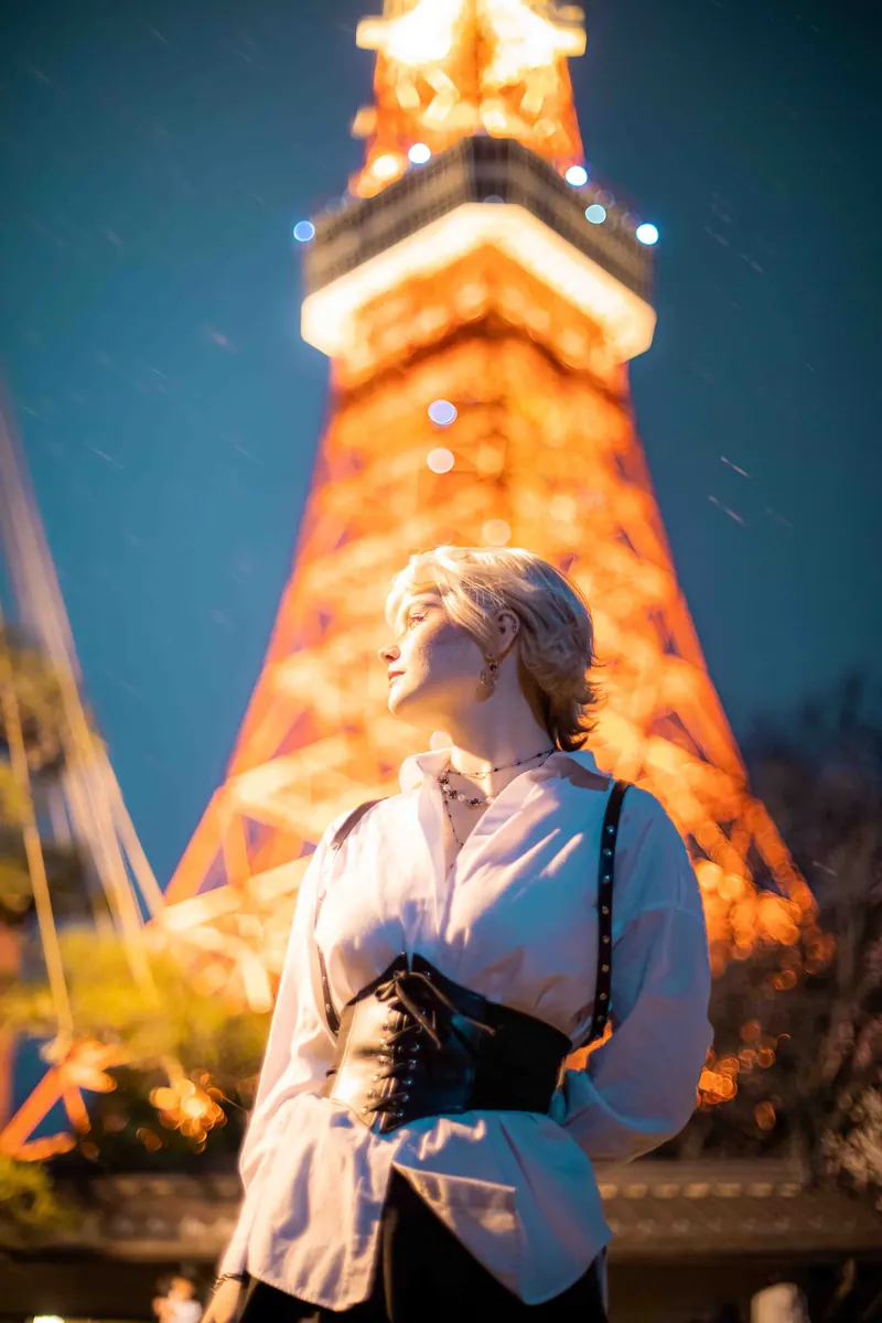 Blonde woman in a white shirt and corset looking up beneath the illuminated Tokyo Tower at night