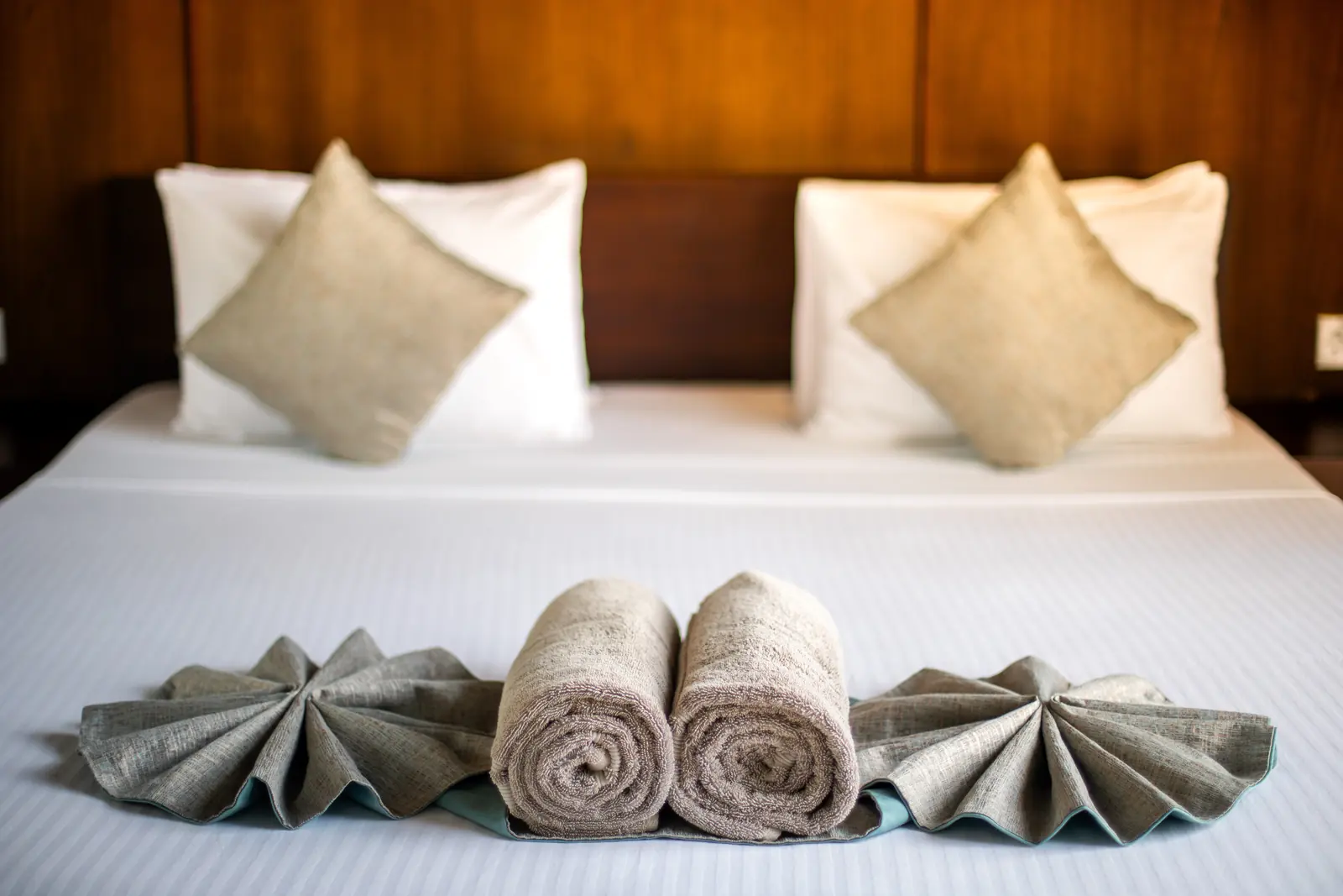 Hotel bed with linen cushions and towels folded as a styling detail