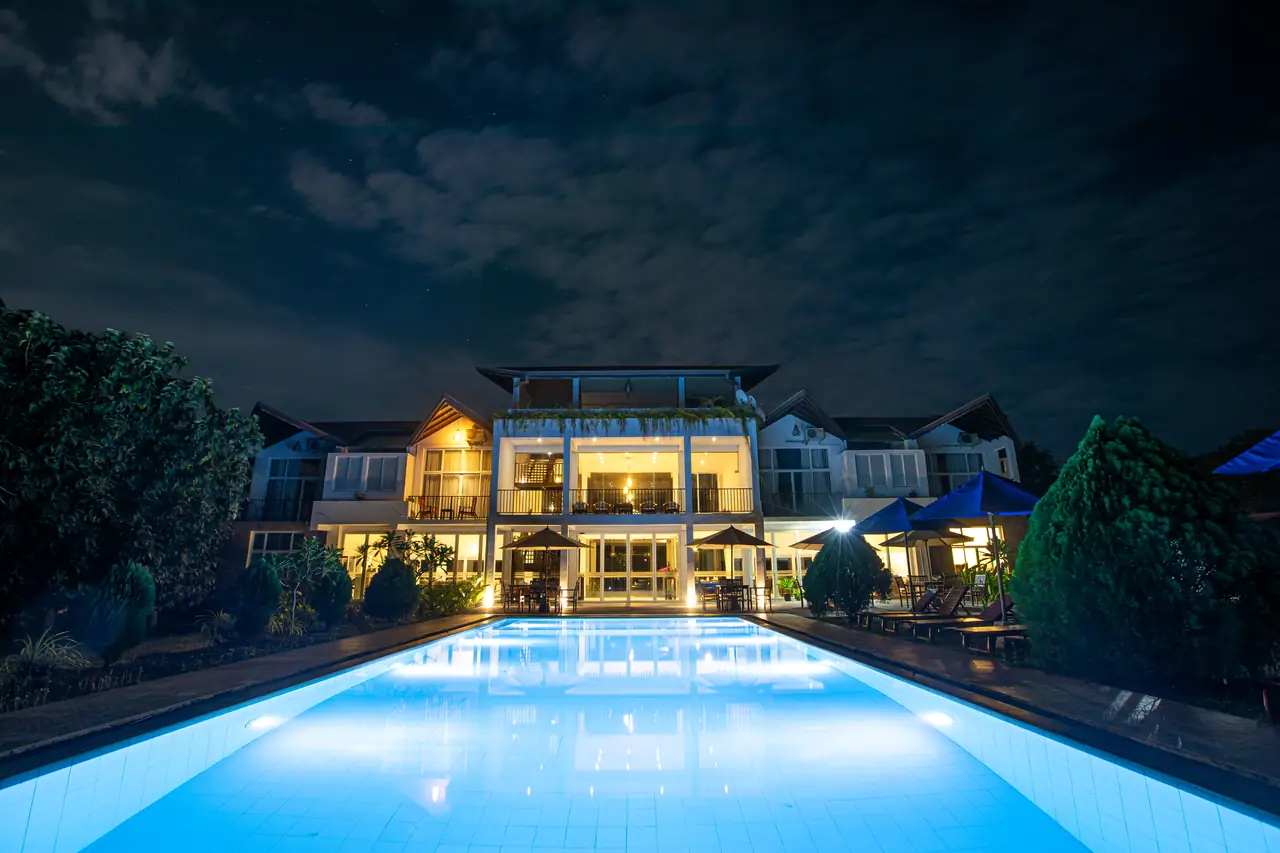 Hotel swimming pool glowing blue at dusk in front of a softly lit building