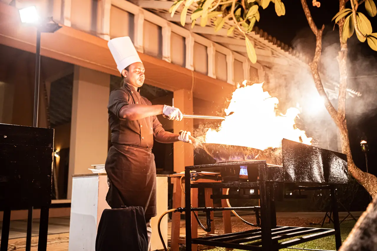Chef working a live-fire grill with tall flames in a hotel restaurant at night