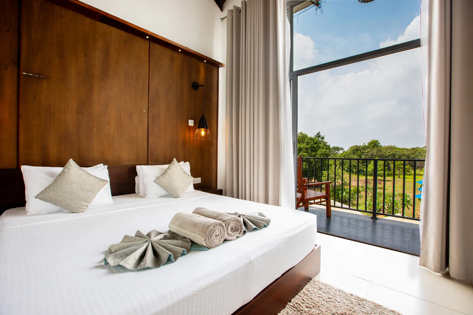 Hotel room with a made bed, folded towel details and a balcony view in natural light