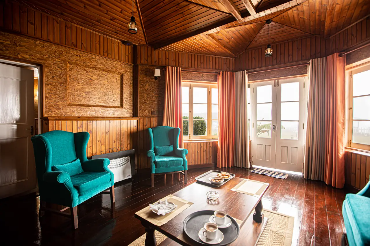Timber-panelled hotel suite with teal armchairs and tall windows