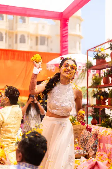 Serene laughing with arms raised as marigold petals fall at the haldi