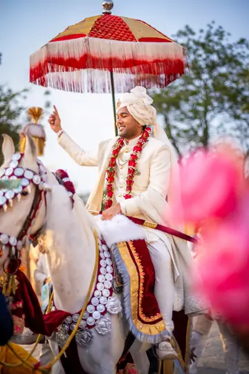 Jay riding a decorated white horse beneath a red ceremonial umbrella