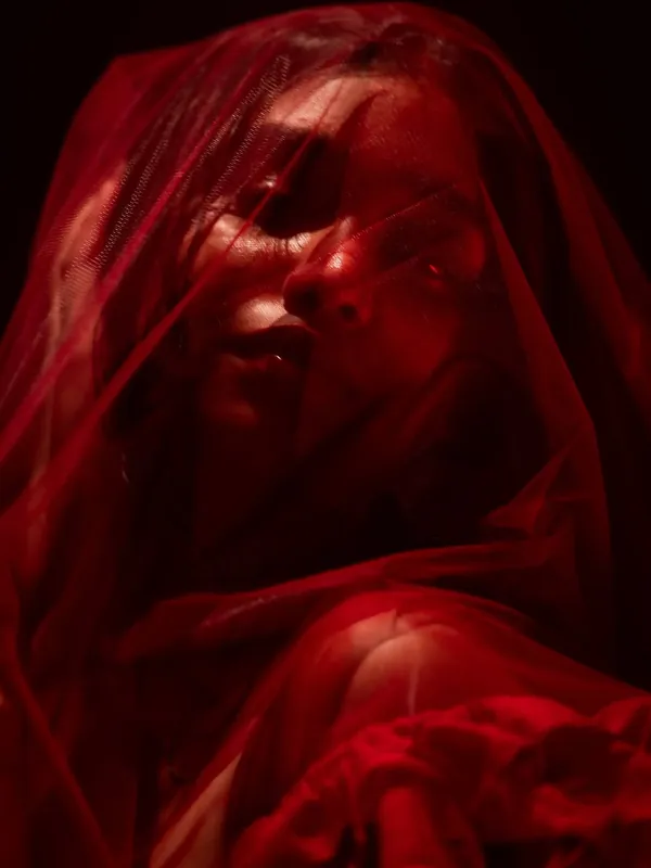 Artistic close-up of a face veiled in sheer red fabric, lit in deep red