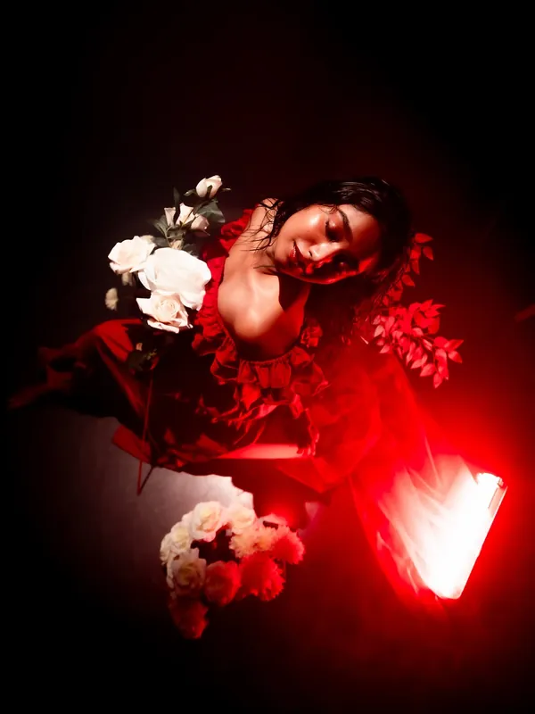 Dreamy studio portrait of a model in a red dress reclining beside white roses under warm red light